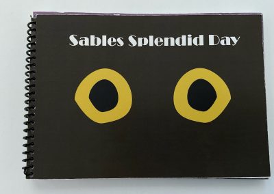 A spiral-bound book cover of a simplified black cat. "Sable's Splendid Day" is at the top of the cover.